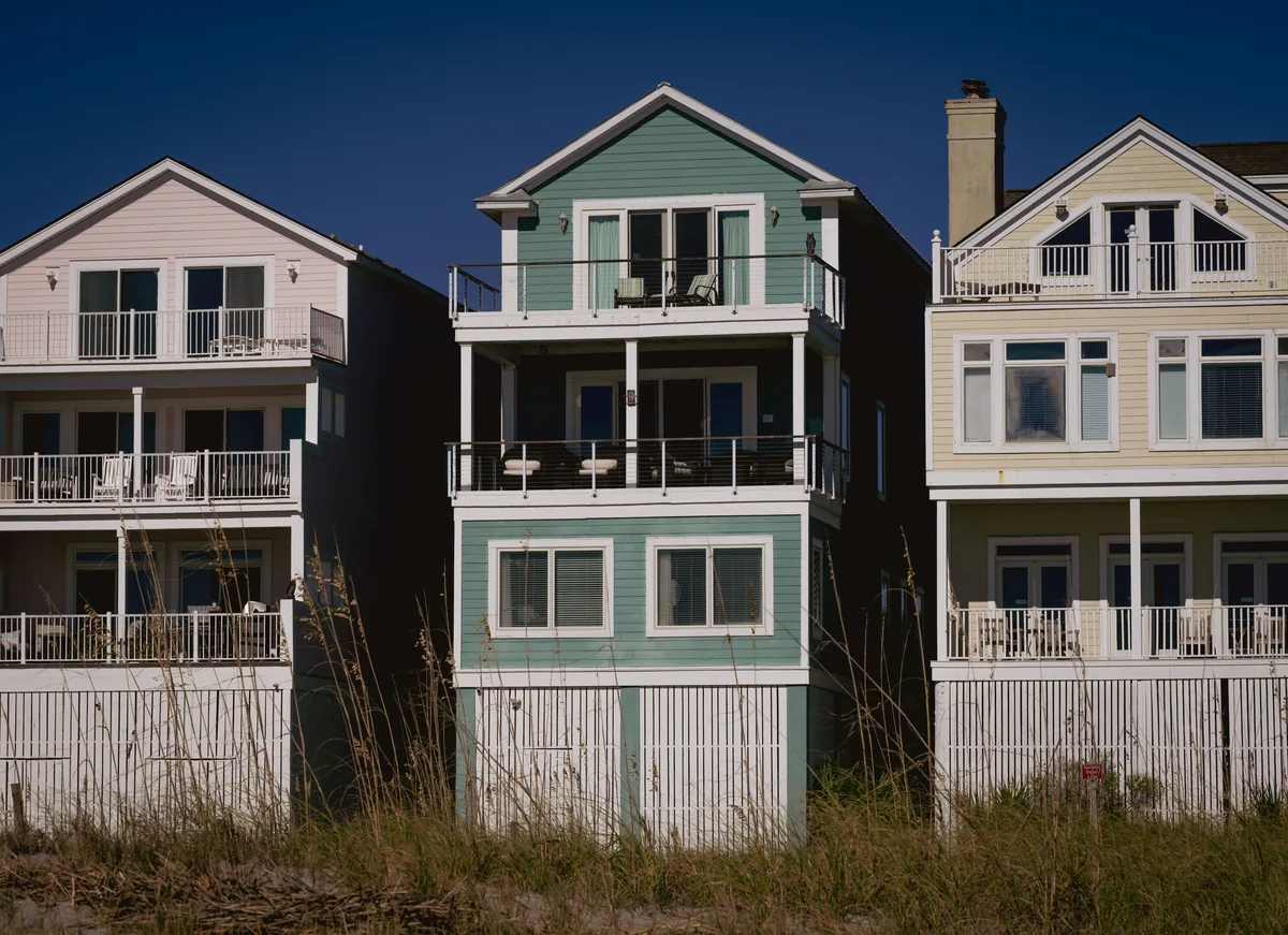 360 Blue management fees, Row of tall pastel beach houses behind a dune fence