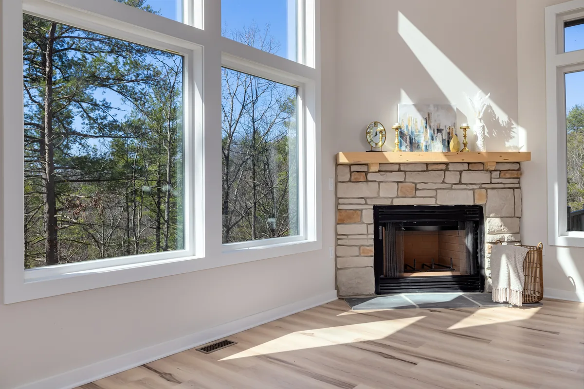 Aspen Luxury Vacation Rentals management fees, Bright room with a stone fireplace and tall windows onto pine trees