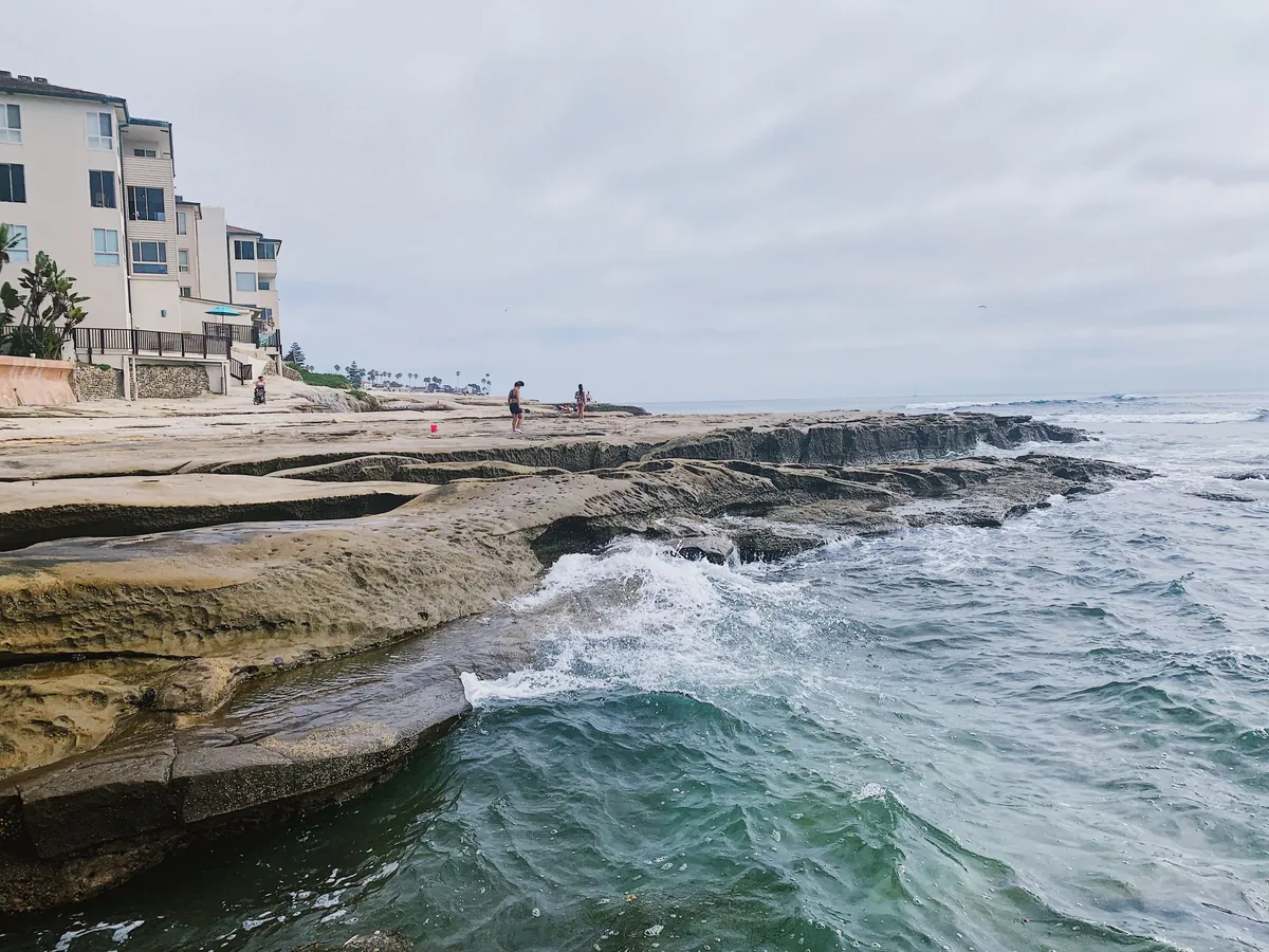 Bluewater Vacation Homes management fees, Waves breaking over a rock shelf below coastal apartment buildings