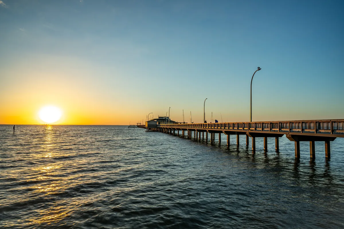Harris Vacations management fees, Sun setting behind a pier stretching across Alabama's bay