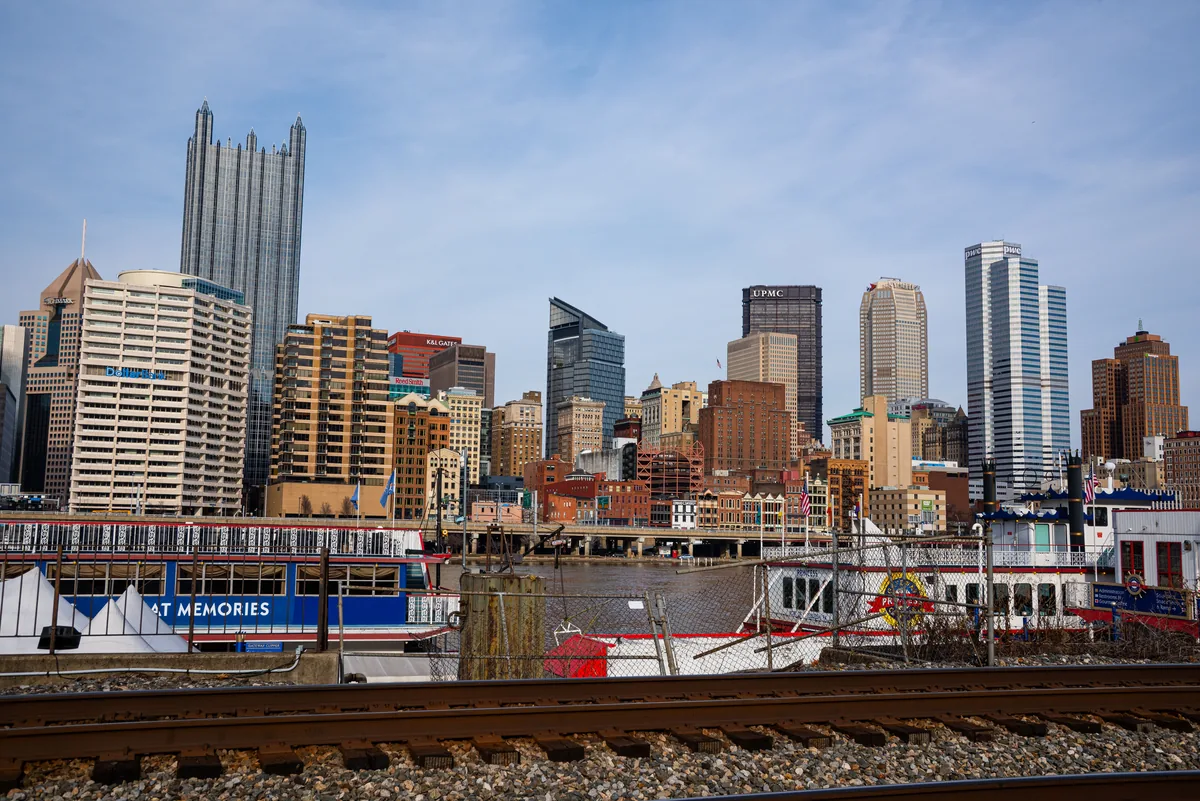 Checkmate Rentals alternatives for Airbnb owners, Pittsburgh skyline rising beyond railway tracks and riverside boats