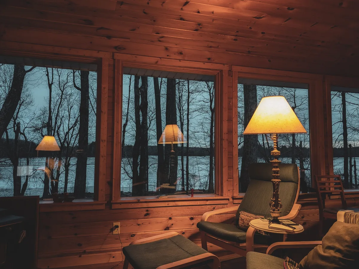 Pocono Lodging Co. management fees, Timber-lined cabin room with lamps lit and windows onto the woods