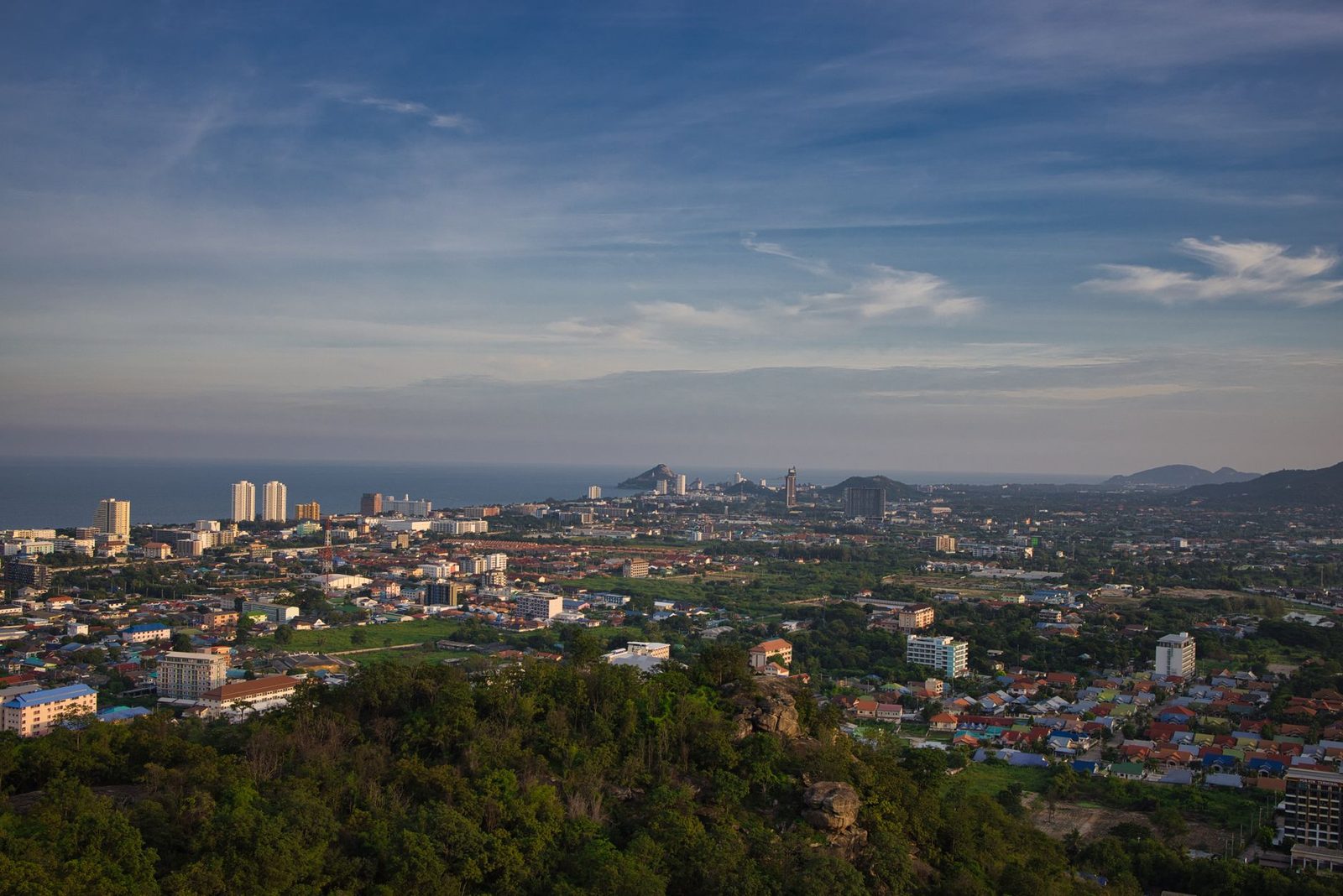 An aerial view of a coastal town spread along a bay below wooded hills