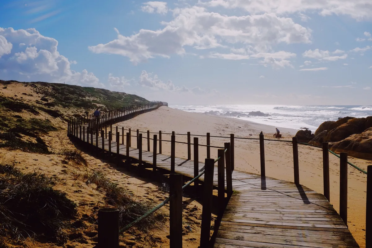 A timber boardwalk running along the dunes above a surf beach