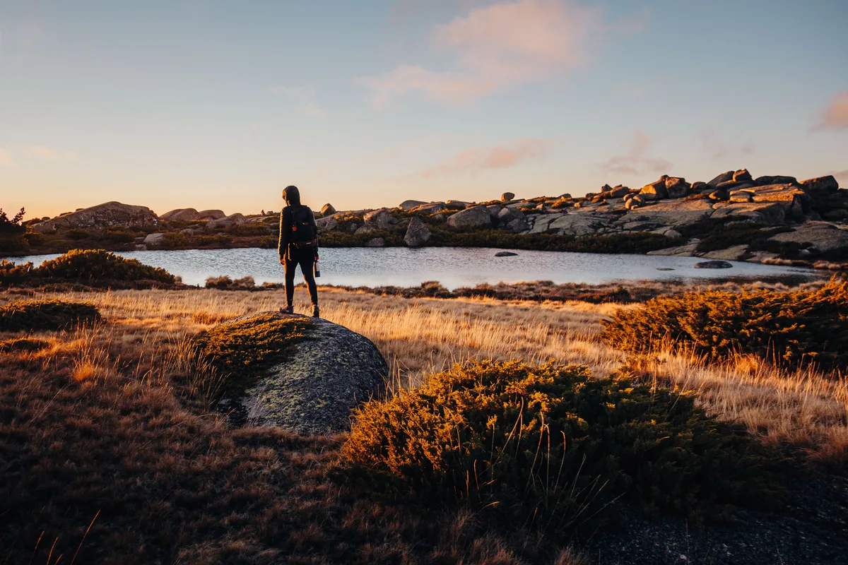 A walker silhouetted beside a mountain lake on the Serra da Estrela