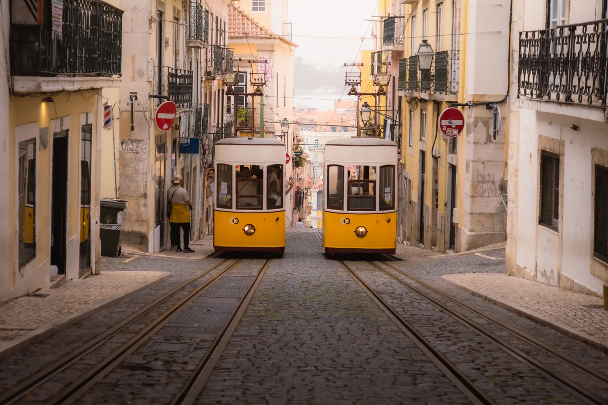 Two yellow trams passing on a cobbled Lisbon street
