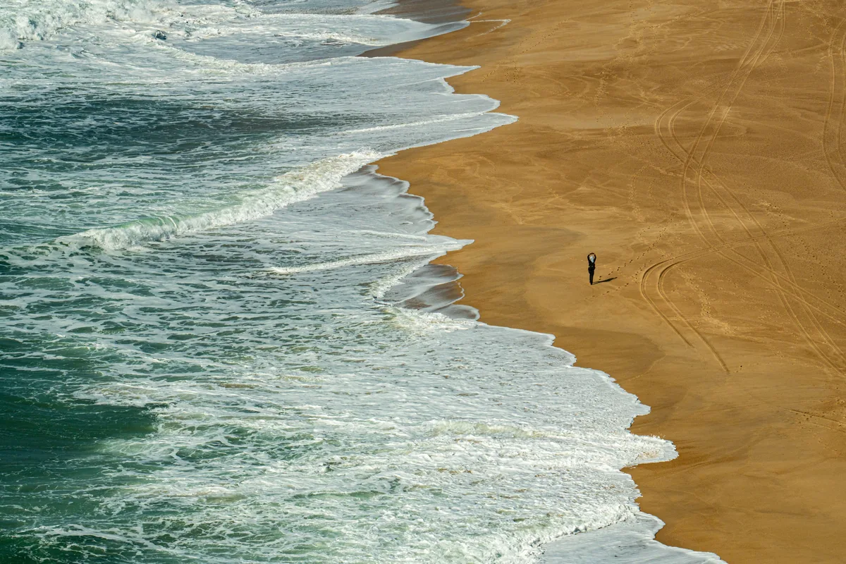 A single figure on a wide sand beach with breaking surf