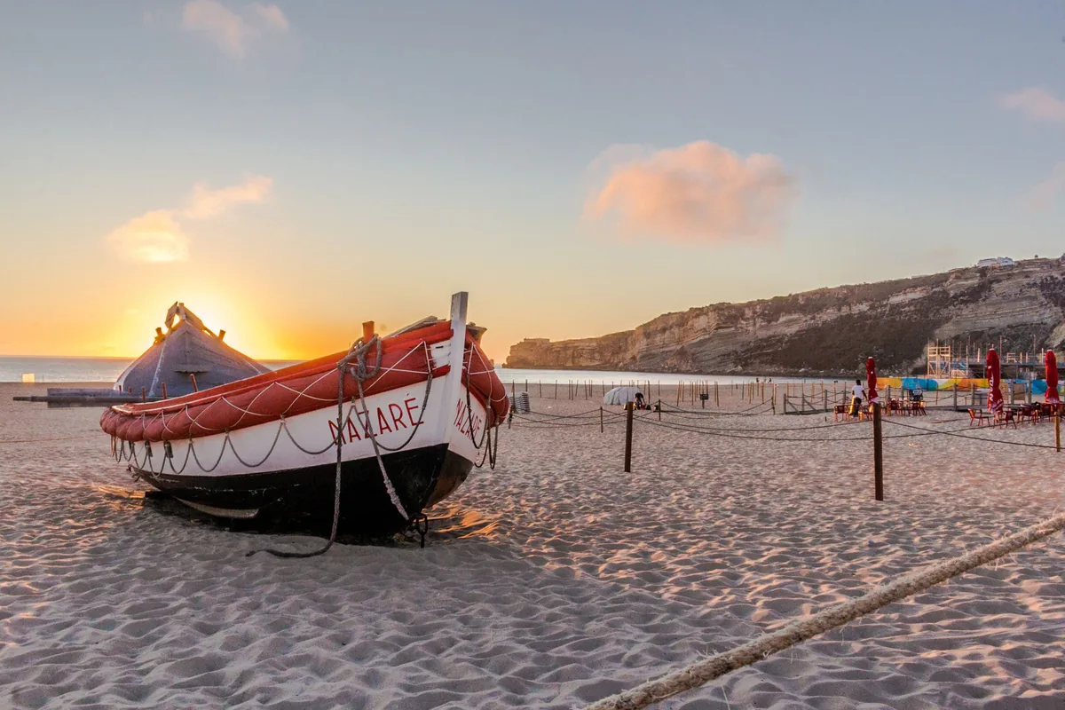 A traditional red and white fishing boat on the sand at Nazare at sunset