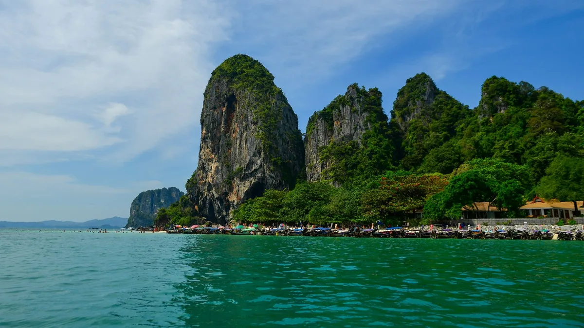 Ao Nang property management, karst headland above turquoise water with longtail boats moored below