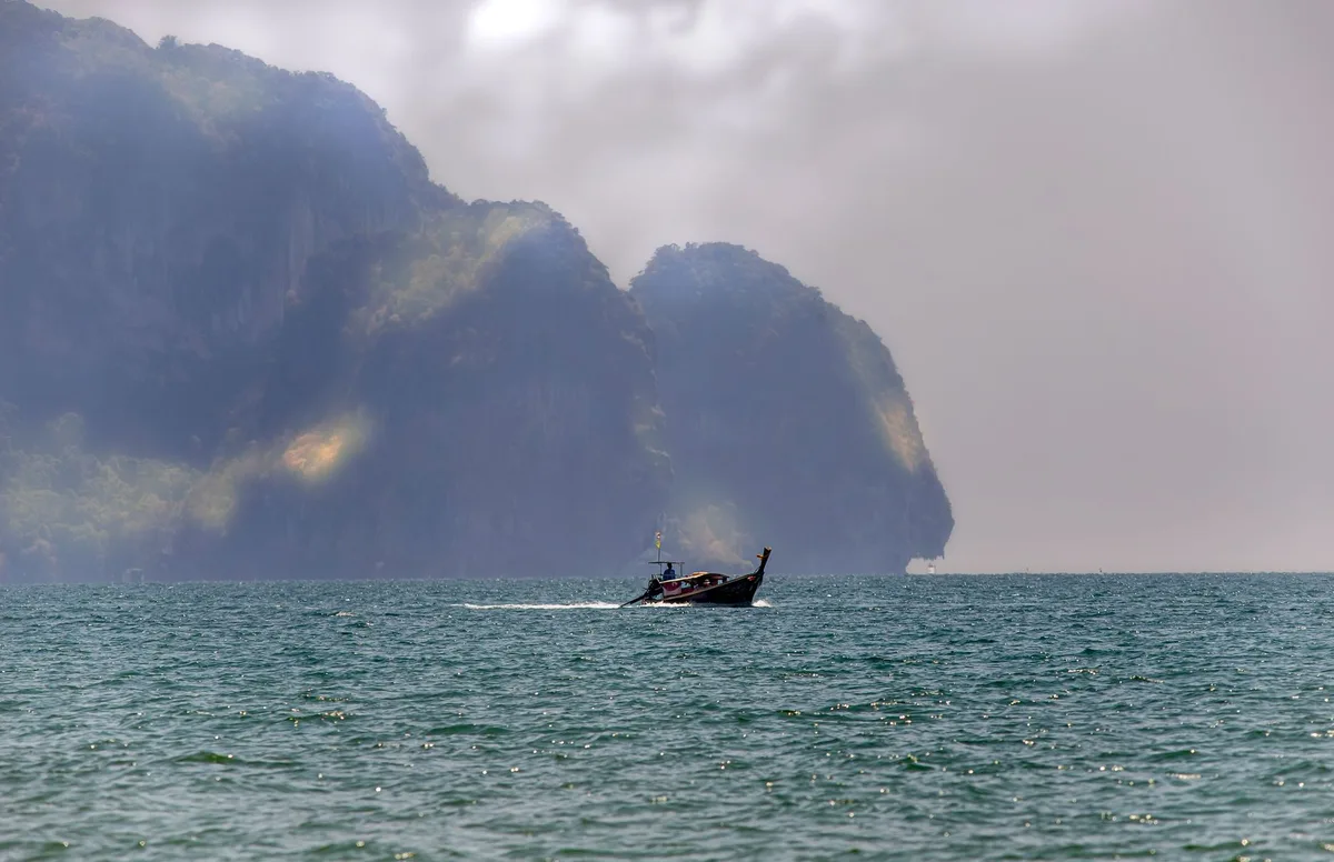 A longtail boat crossing below an Andaman limestone island