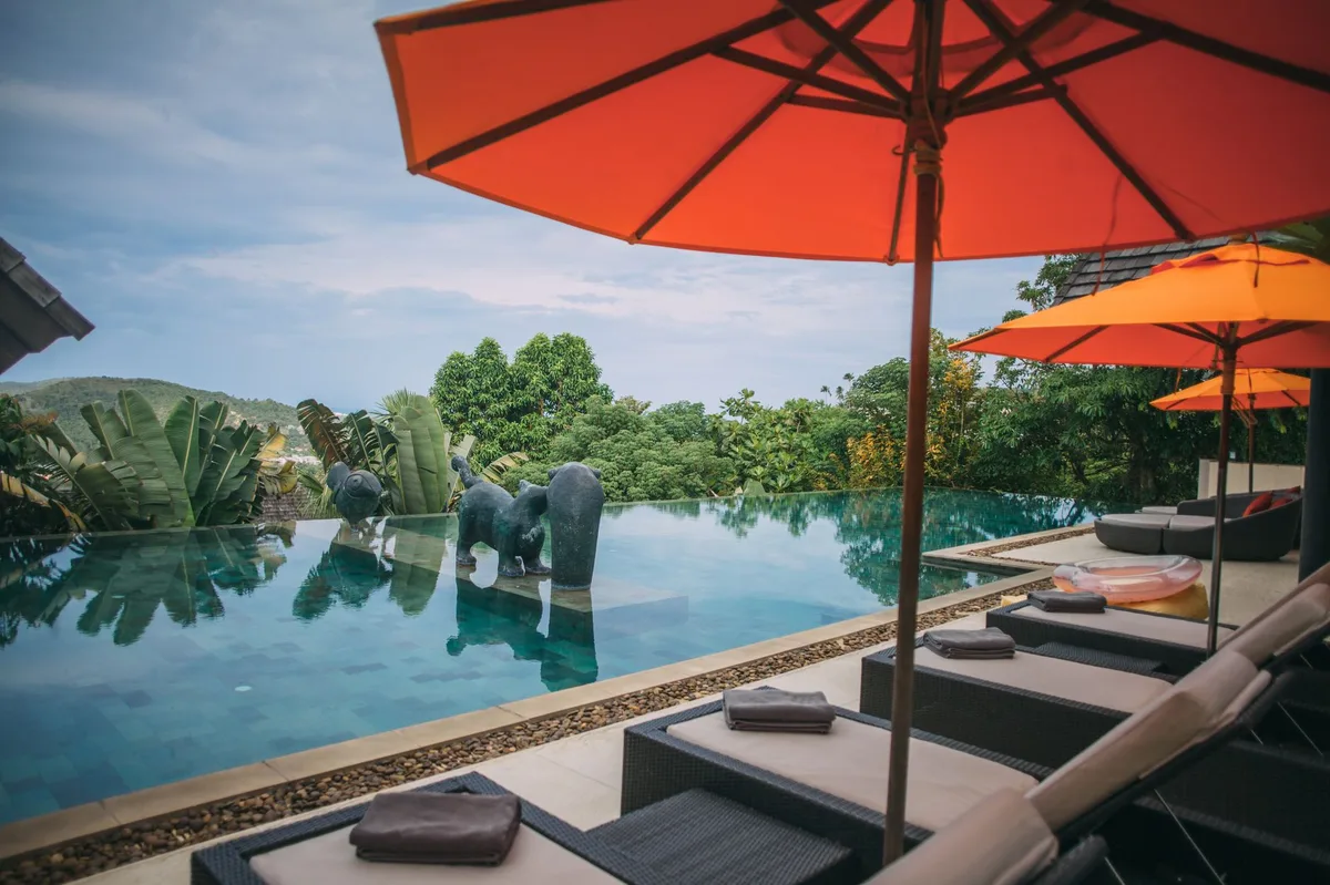 Phuket villa rental management, infinity pool with red parasols and Thai elephant statues