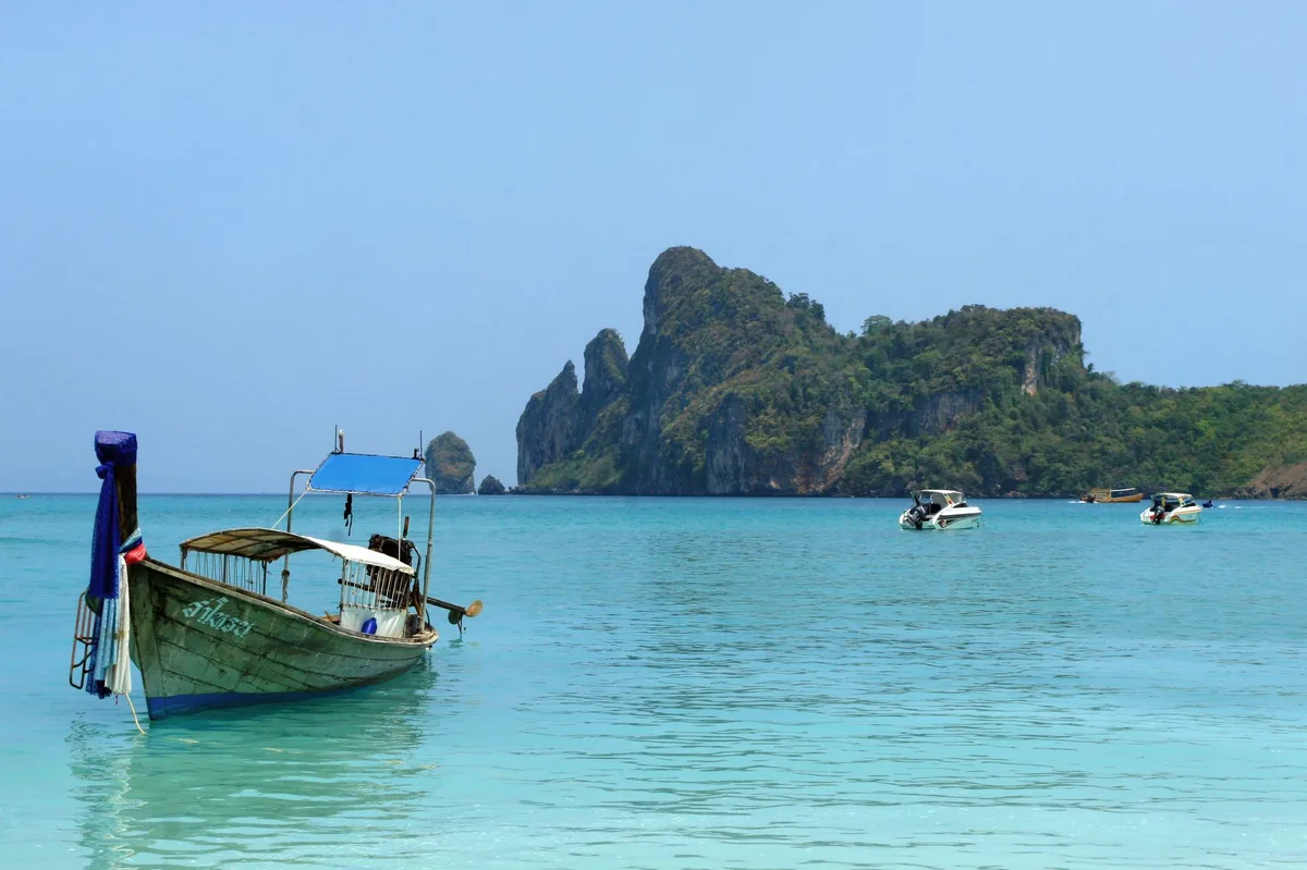 Thailand vacation rental management, longtail boat moored below limestone cliffs