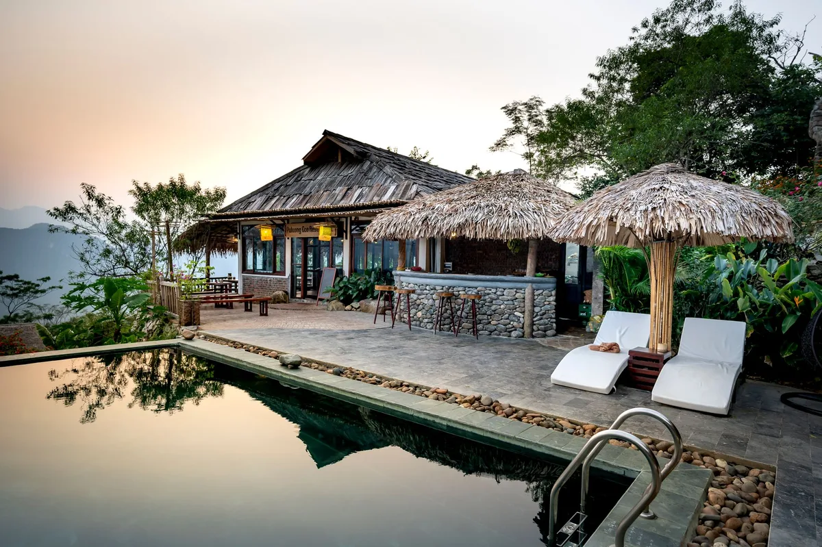 An infinity pool and thatched pavilion above a wooded valley