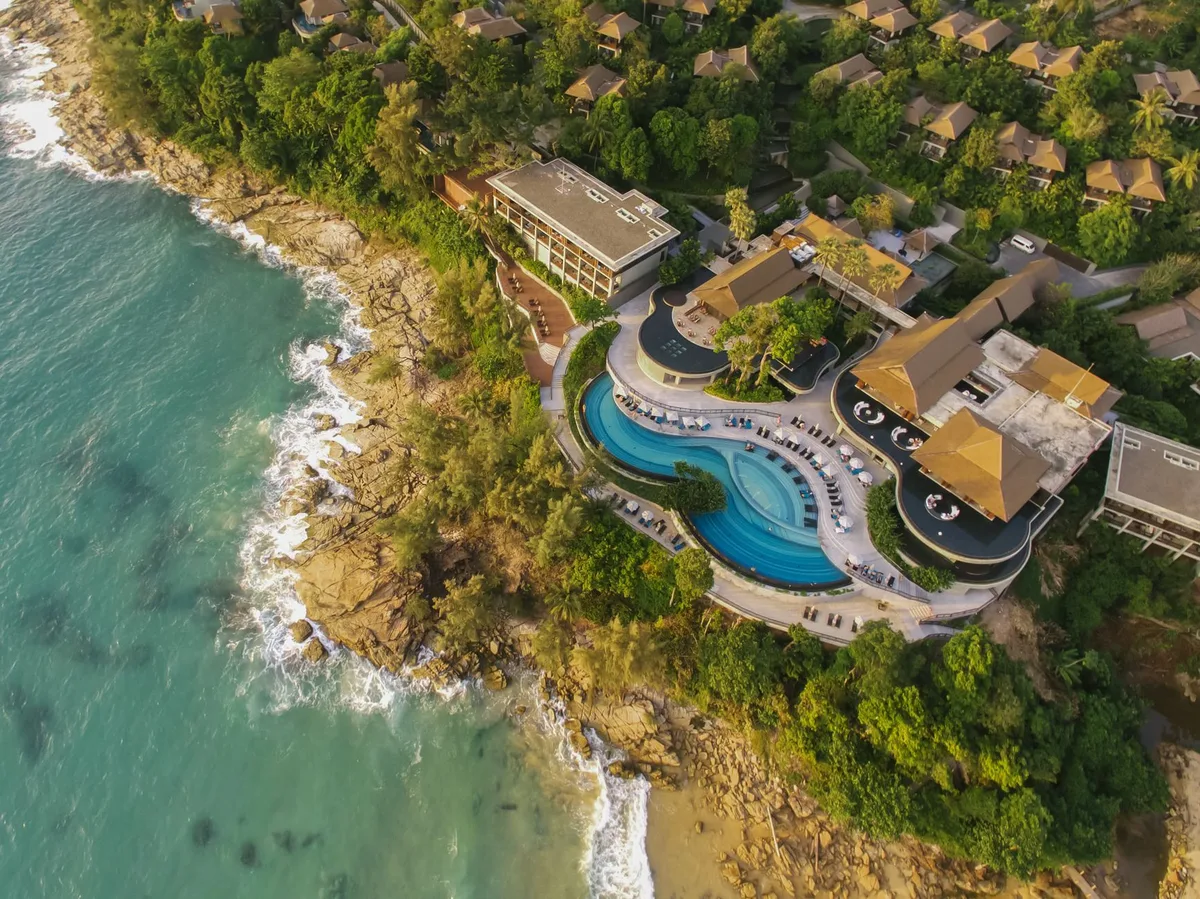 An aerial view of a resort with curving pools on a wooded headland