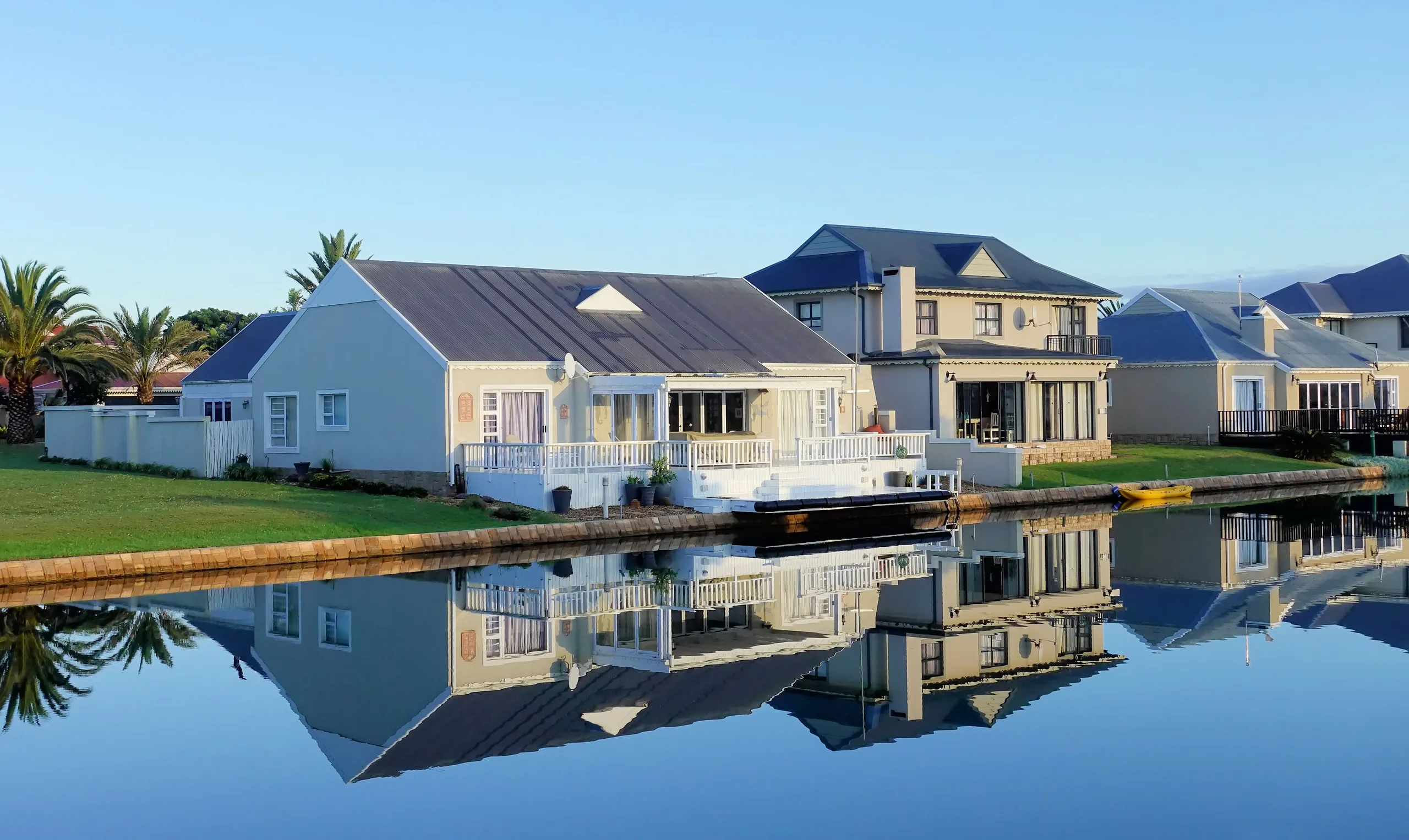 Waterfront homes reflected in calm water on a sunny day