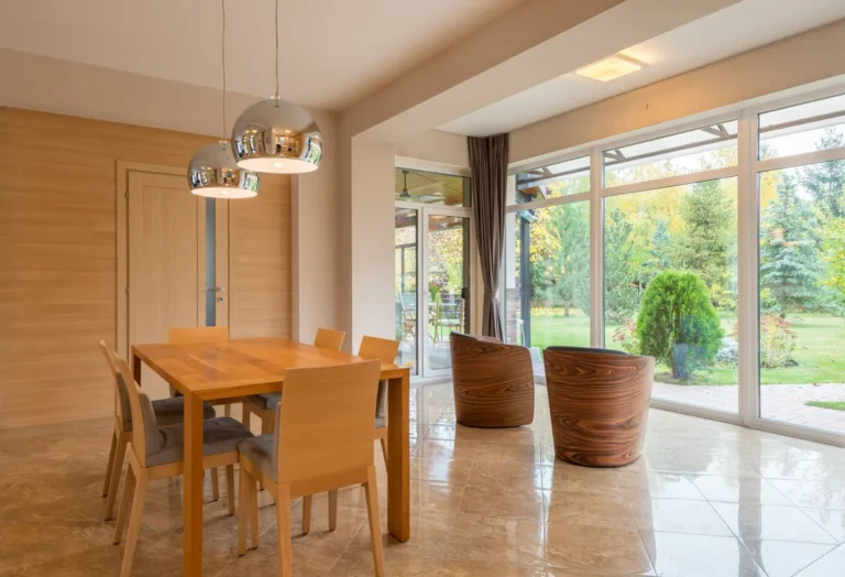 Dining table with wooden chairs beside large garden windows