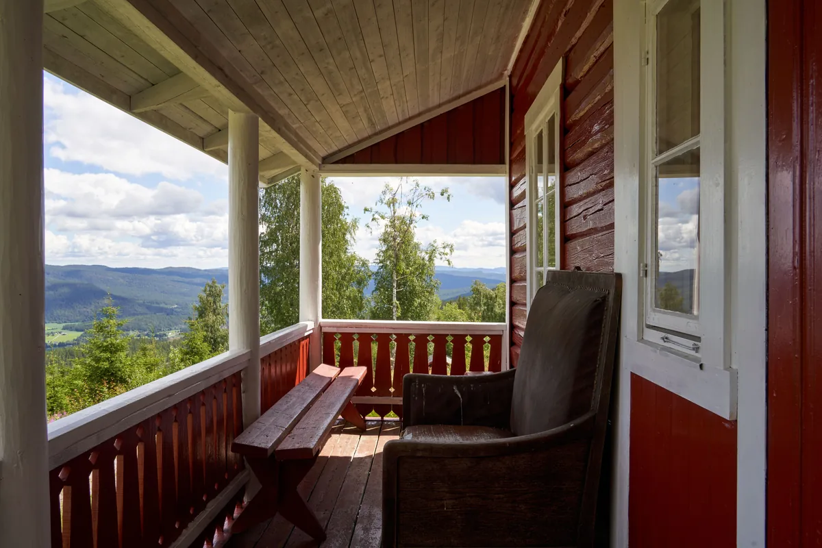 Covered wooden porch with a bench and armchair overlooking forested hills