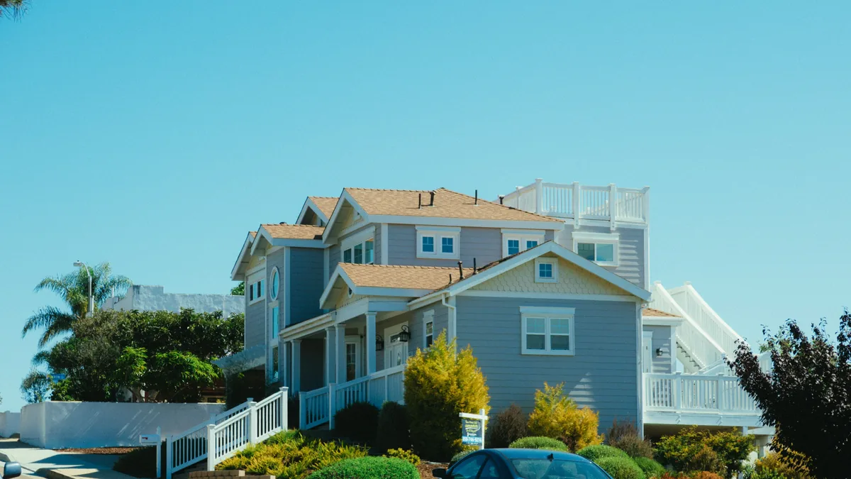 Blue two-storey house with palm trees and a white fence